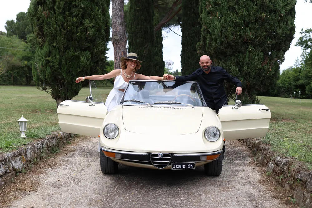 Alessandro In Testa, parrucchiere a Roma Nord: uomo e donna su un'auto d'epoca bianca